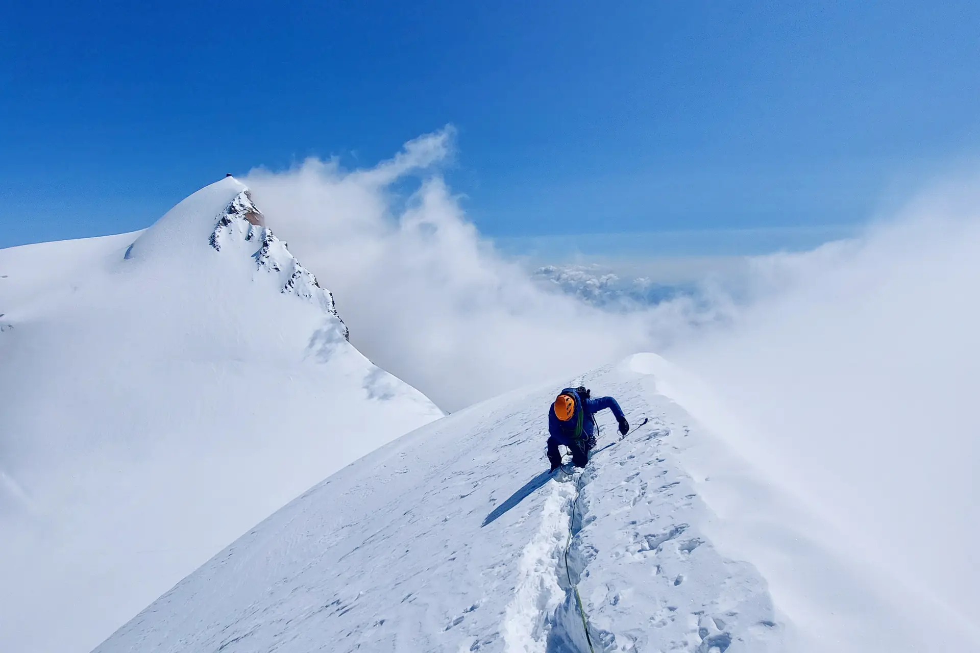 Alpiniste encordé sur une arête de neige, en direction du sommet